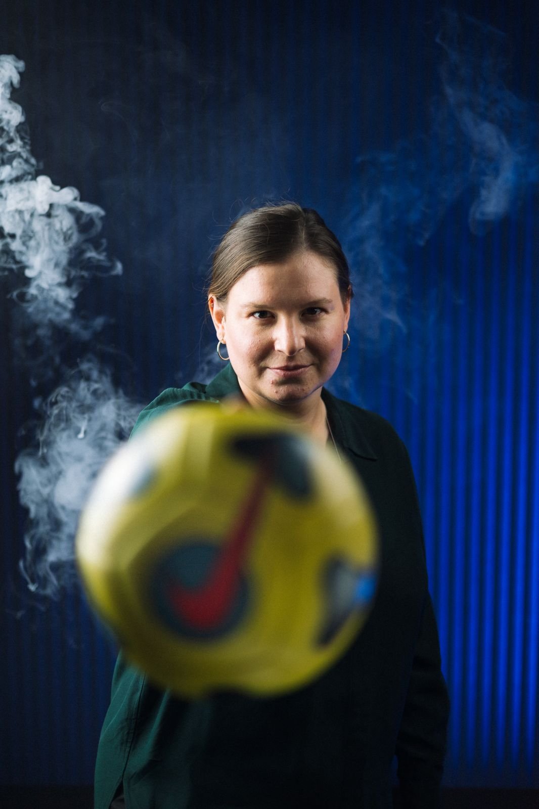 Grace Parker of Understand Your Group holding a yellow soccer ball with smoke in the background.